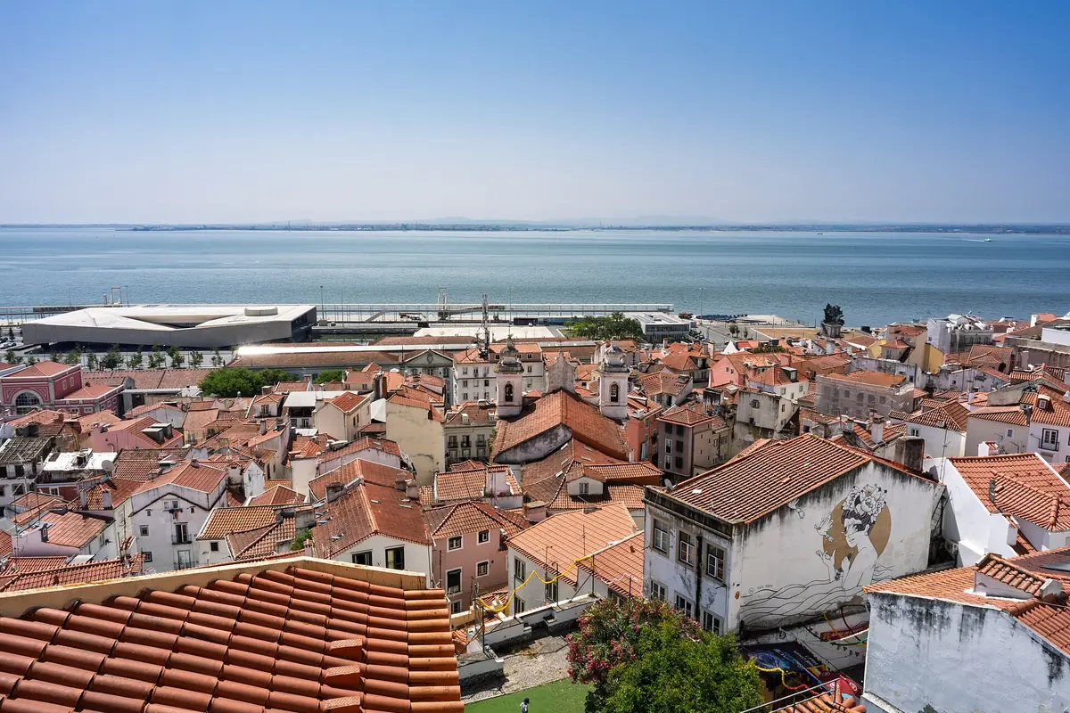 A wide view over the red-tiled roofs of Alfama from the Santa Luzia viewpoint, with the Tagus river beyond