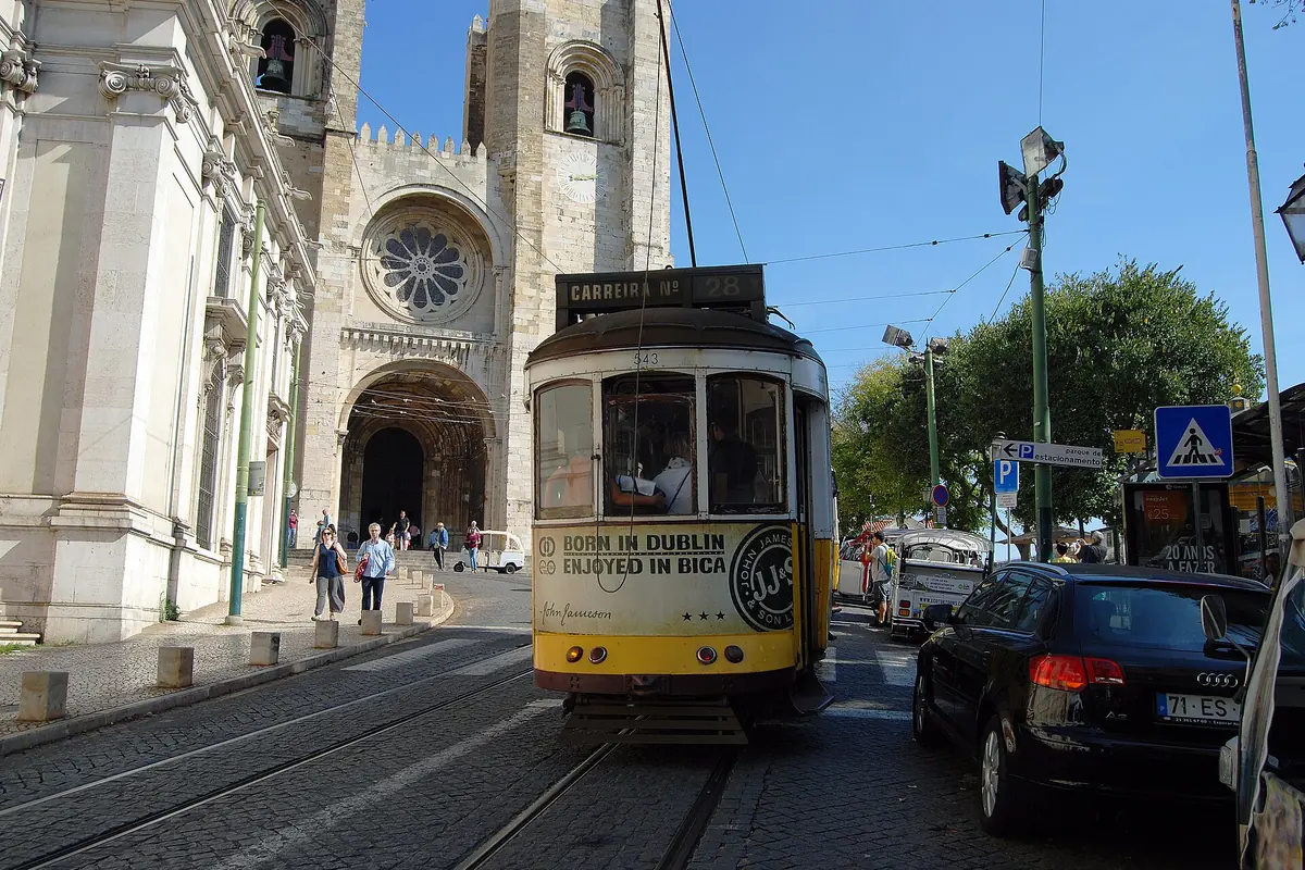 A yellow tram passes below the twin towers of Lisbon Cathedral, the Sé, on a sunny street