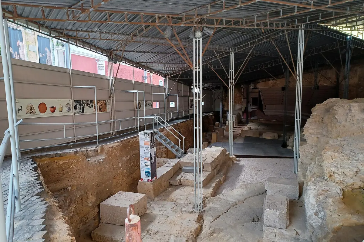 Rough stone blocks and steps of the Roman theatre in Lisbon seen from a walkway below a steel roof