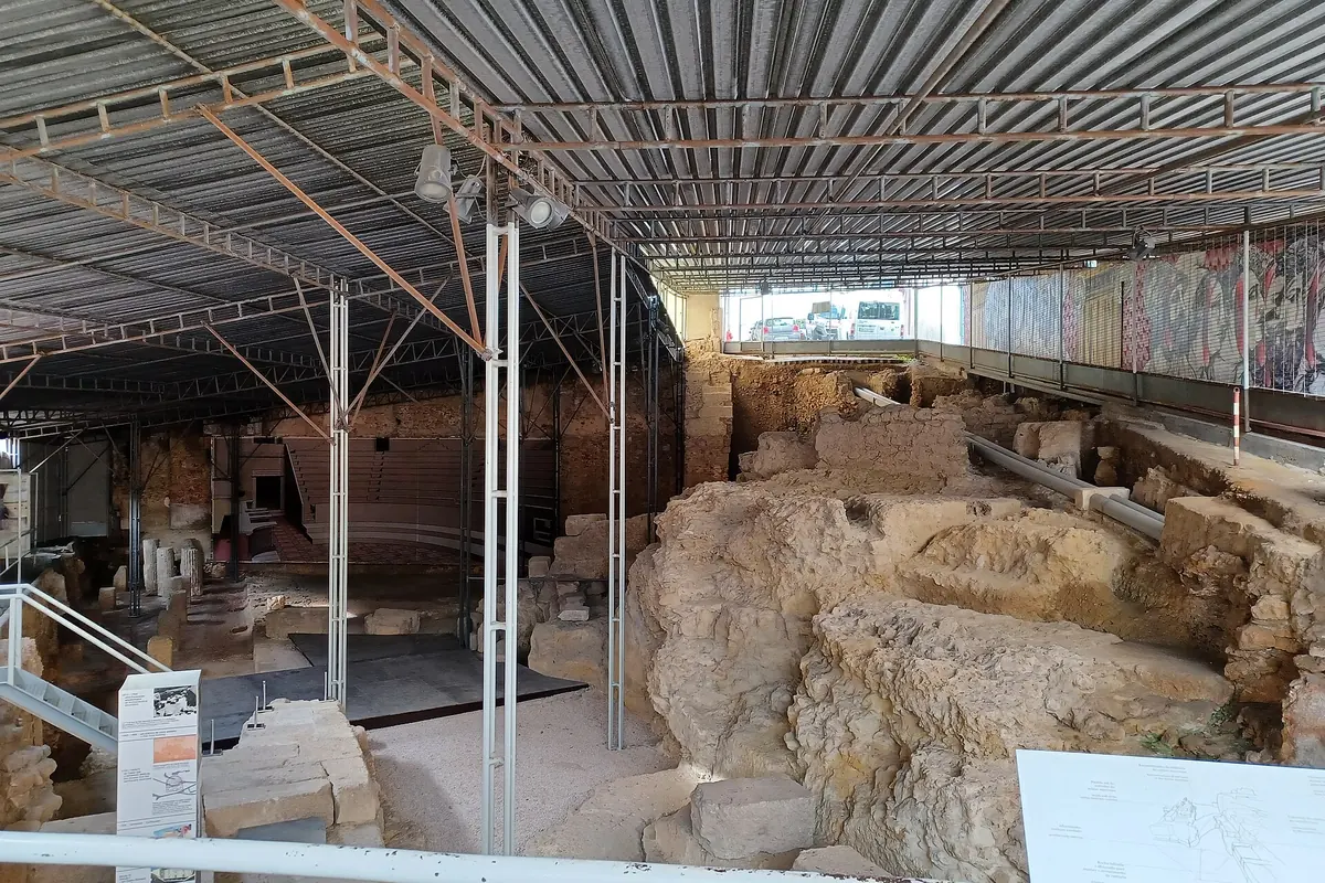 Ruins of the Roman theatre of Lisbon under a long steel and mesh roof, with excavated stonework below a walkway