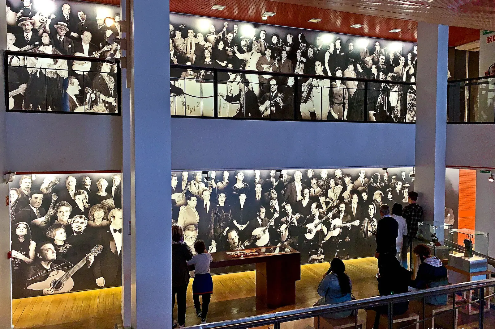 A gallery at the Museu do Fado in Lisbon with a tall wall of black-and-white photographs of fado audiences and guitarists